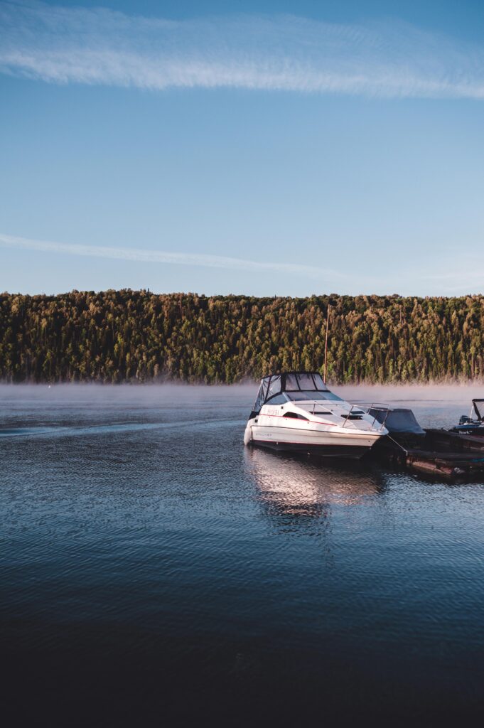 Serene scene of a motorboat moored on a tranquil river in Bashkortostan with misty hills in the background.
